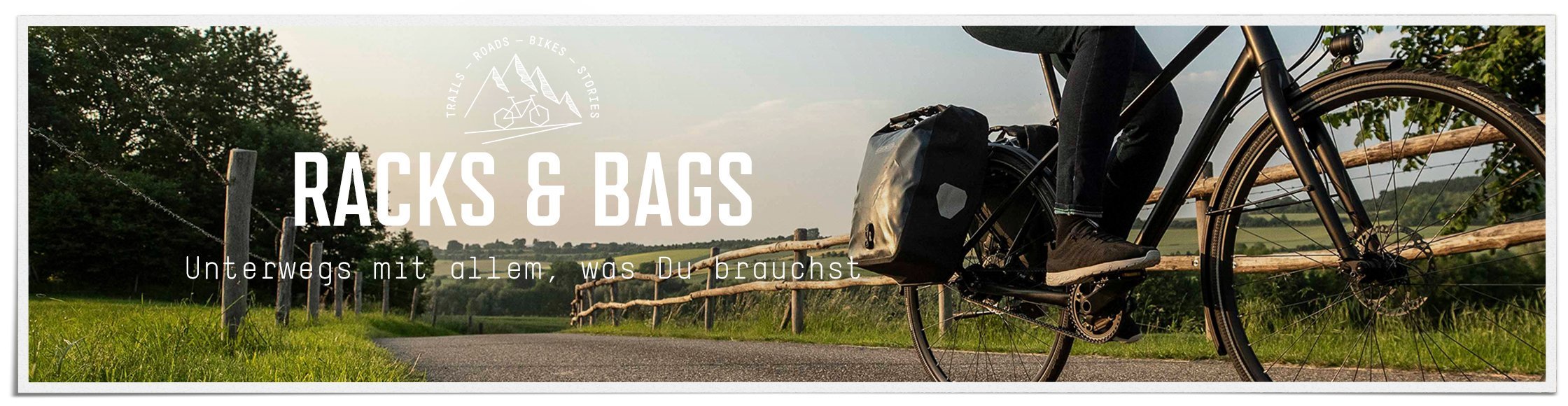 Racks & Bags: Radfahrerin radelt auf einer ruhigen, asphaltierten Straße in der Natur mit zwei großen Ortlieb-Gepäcktaschen am Gepäckträger