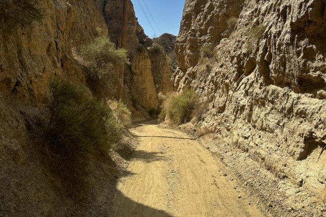 Ein staubig-sandiger Canyon. Eine Telegrafenleitung säumt die enge Schotterstraße, ein kleiner Fleck blauen Himmels ziert den oberen Bildrand.