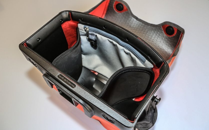 The interior of a red Ortlieb bicycle bag with multiple compartments, including a padded area and a small zippered pocket.