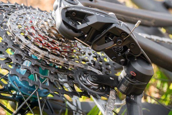 Ein SRAM Transmission T90 Schaltwerk von unten fotografiert. Man sieht das Ende eines Bowdenzugs und in der Unschärfe die Ritzelkassette und Teile von Fahrrad und Hinterrad.