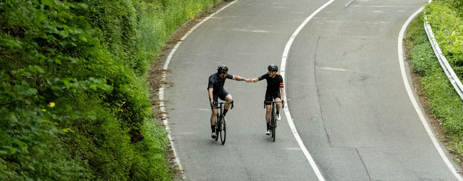 Two road cyclists on Specialized Tarmac SL7 bikes shake an appreciative fist at each other after completing the climb.