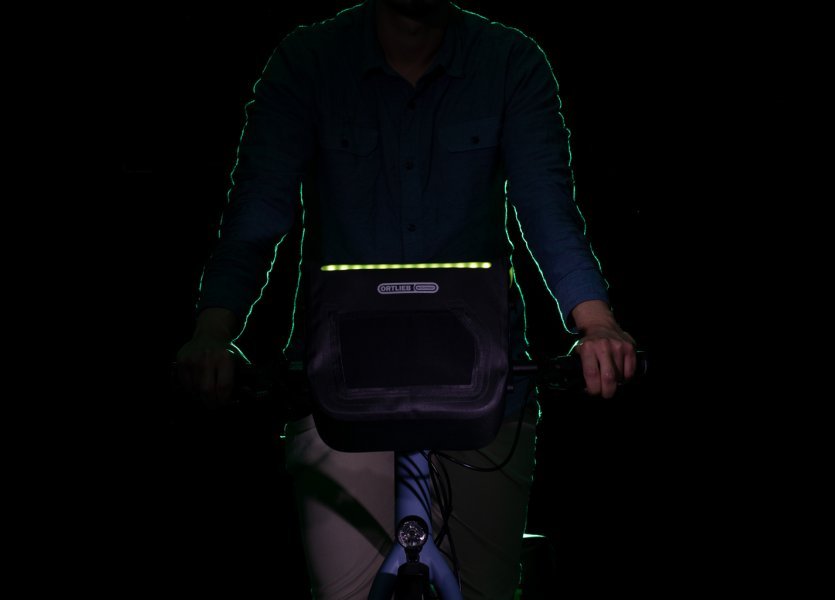 Fahrradfahrer mit montierter ORTLIEB E-Glow Lenkertasche in Dunkelheit – eingeschaltete LED-Beleuchtung sorgt für Sichtbarkeit
