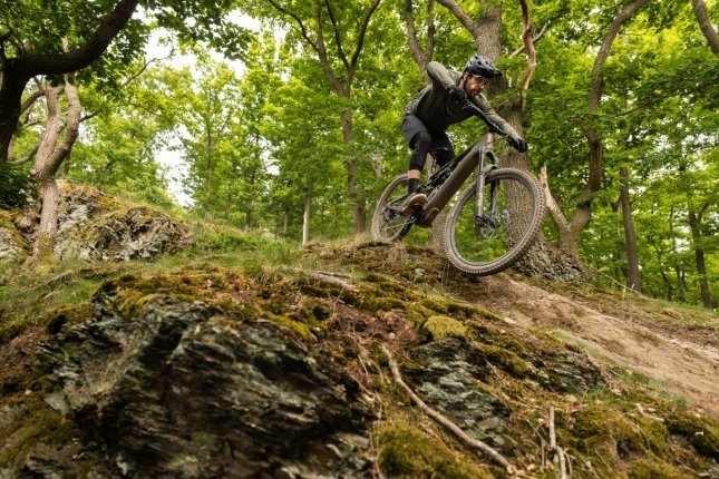 Weitwinkel Foto von unten aufgenommen: Berno heizt mit einem grün-bronzefarbenen E-MTB einen Trail hinab