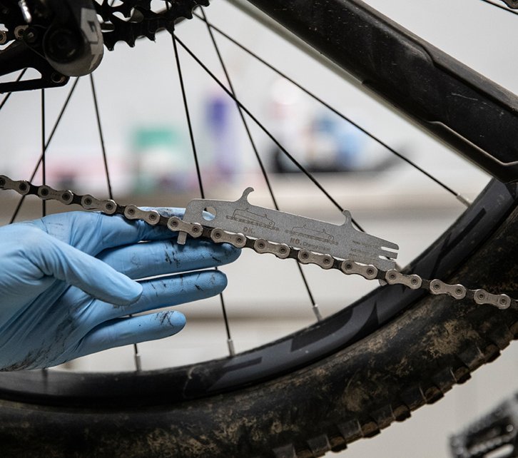 A mechanic measures the condition of the bike chain with a chain wear indicator. 