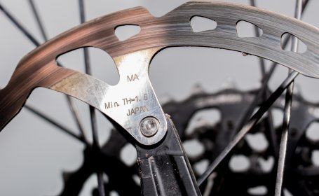 Gros plan sur un disque de frein de vélo usé, avec l’indication d’épaisseur minimale “Min. TH=1.5” et une vis de fixation.