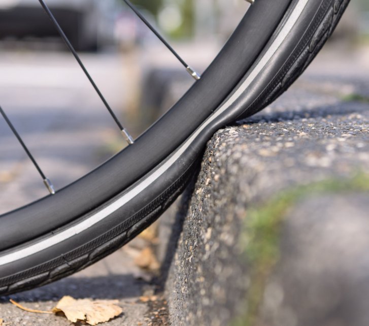 Close-up photo: A bicycle tyre is compressed flat against a kerb all the way to the rim.