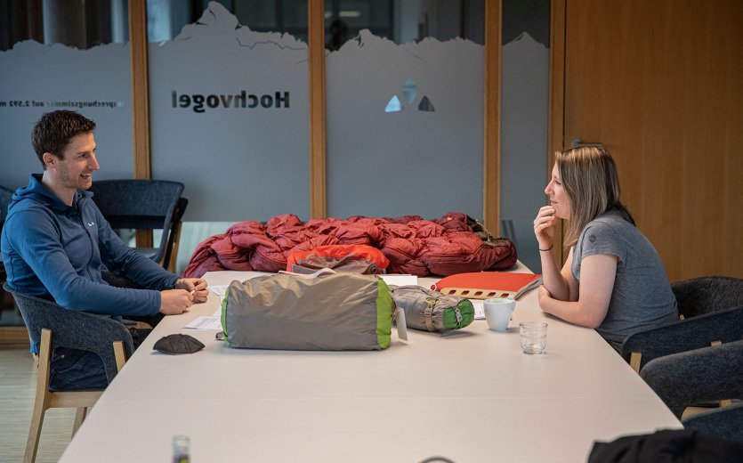 bc-Brandmanagerin Svenja und Vaude-Produktmanager Markus im Gespräch an einem Tisch. Vor ihnen liegen Zelte, Isomatten und Schlafsäcke.