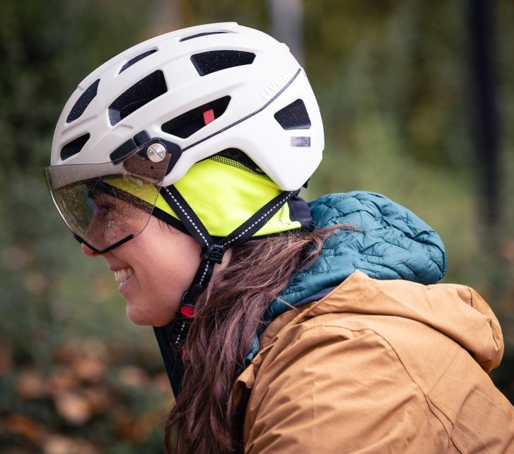 Side view of a young woman wearing a white bicycle helmet with a flip-up visor.