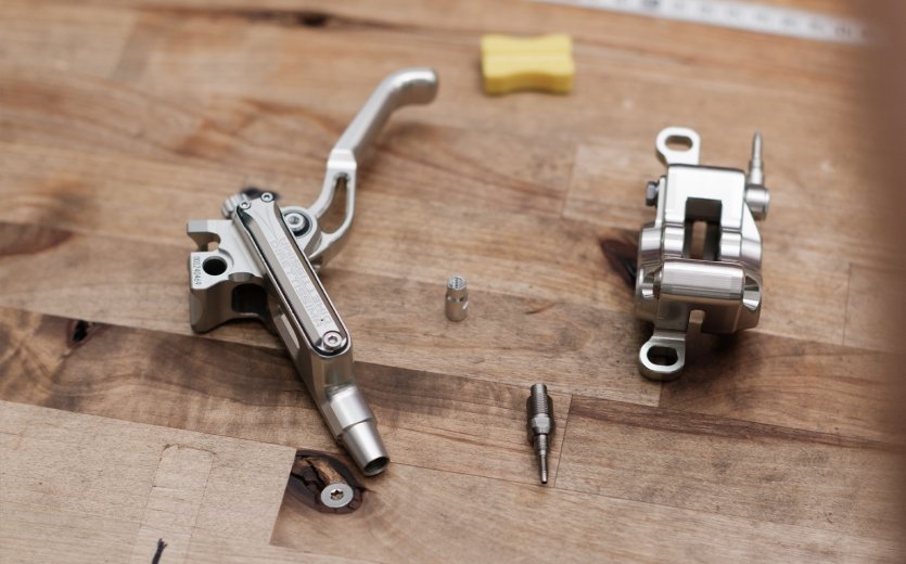 Components of a Trickstuff brake meticulously arranged on a wooden workbench, showcasing high-quality craftsmanship.