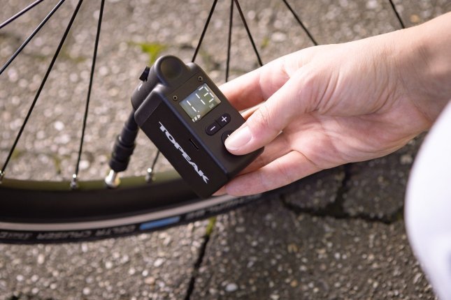 Close-up photo: A battery-powered mini compressor inflates a bicycle tyre.