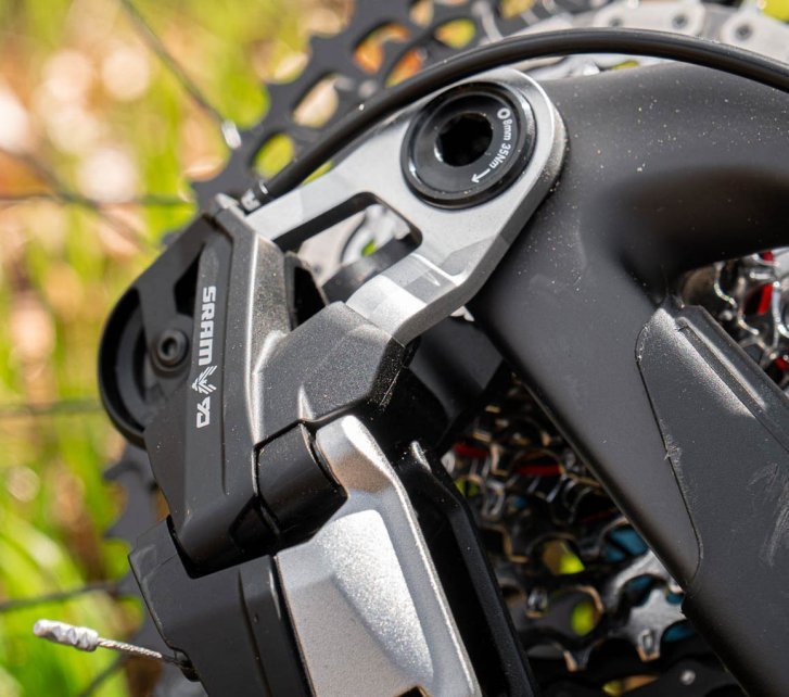Un desviador SRAM Transmission T90 fotografiado desde abajo. Se ve el extremo de una funda de cable y, desenfocados en el fondo, el casete y partes de la bicicleta y la rueda trasera.