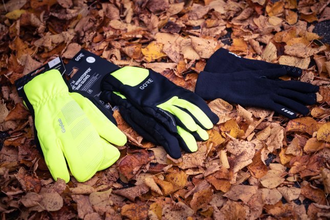 Three pairs of winter cycling gloves lie on brown autumn leaves.
