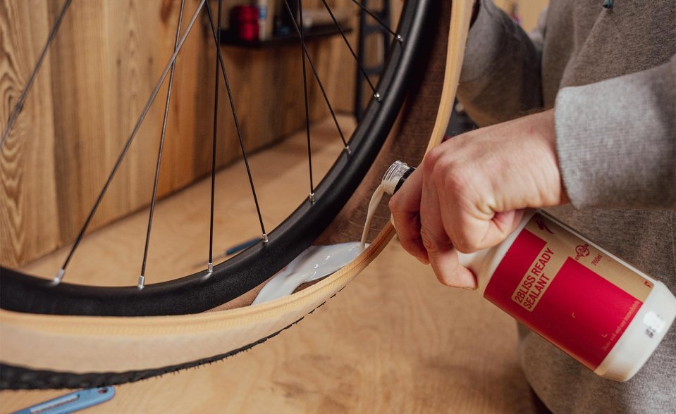 Main versant du liquide préventif dans le flanc ouvert d’un pneu déjà monté sur la jante.