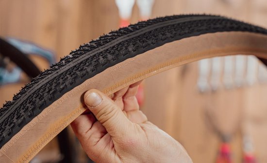 Main tenant un pneu gravel Specialized Pathfinder, avec la flèche indiquant le sens de rotation visible sur le flanc.