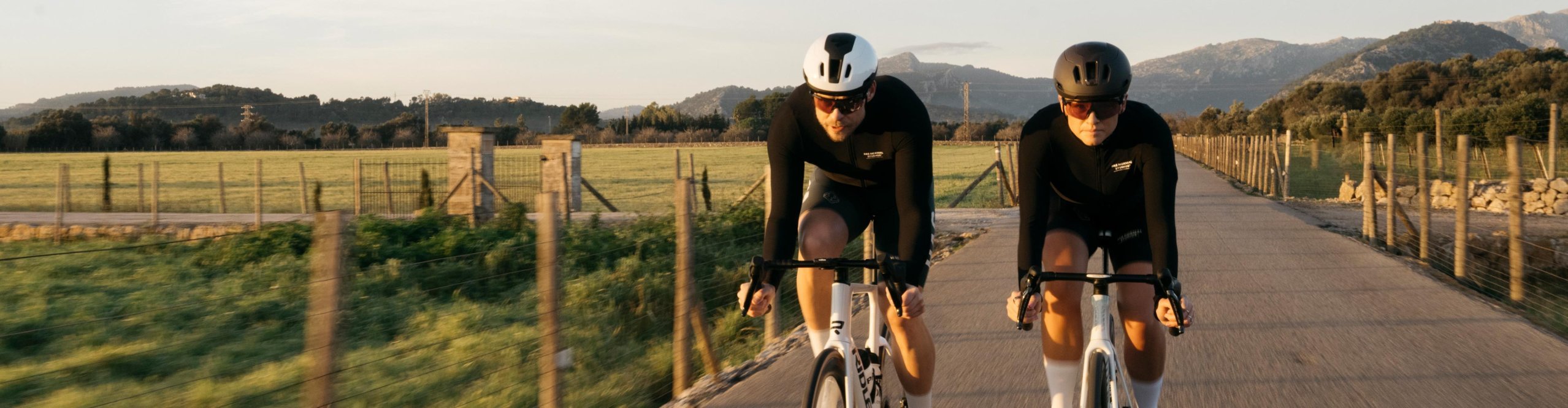 Deux cyclistes sur route avec des casques Sweet Protection roulent sur une route rurale de Majorque en fin de journée.