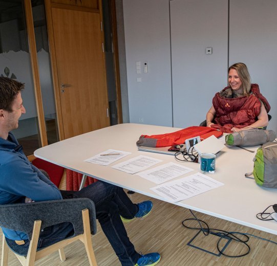 bc-Brandmanagerin Svenja mit Schlafsack und Vaude-Produktmanager Markus im Gespräch an einem Tisch.