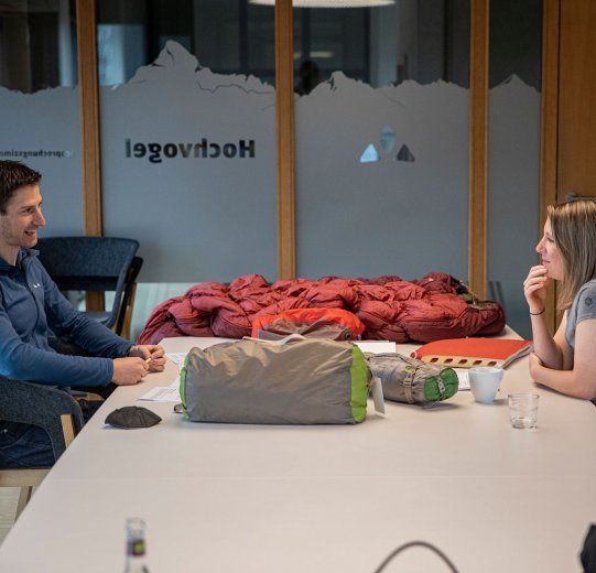 bc-Brandmanagerin Svenja und Vaude-Produktmanager Markus im Gespräch an einem Tisch. Vor ihnen liegen Zelte, Isomatten und Schlafsäcke.