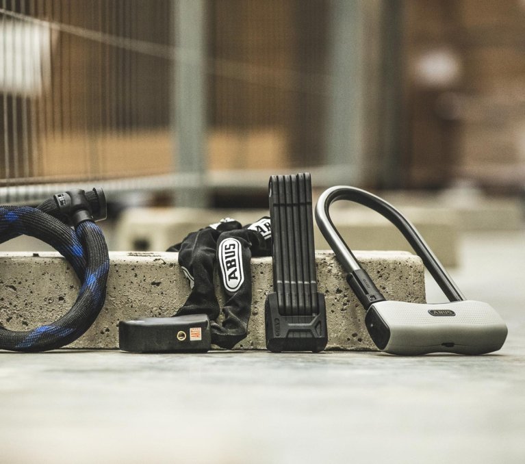 Varios candados para bicicleta – de cable, cadena, plegable y en U – colocados uno junto a otro sobre un bloque de hormigón en entorno urbano.