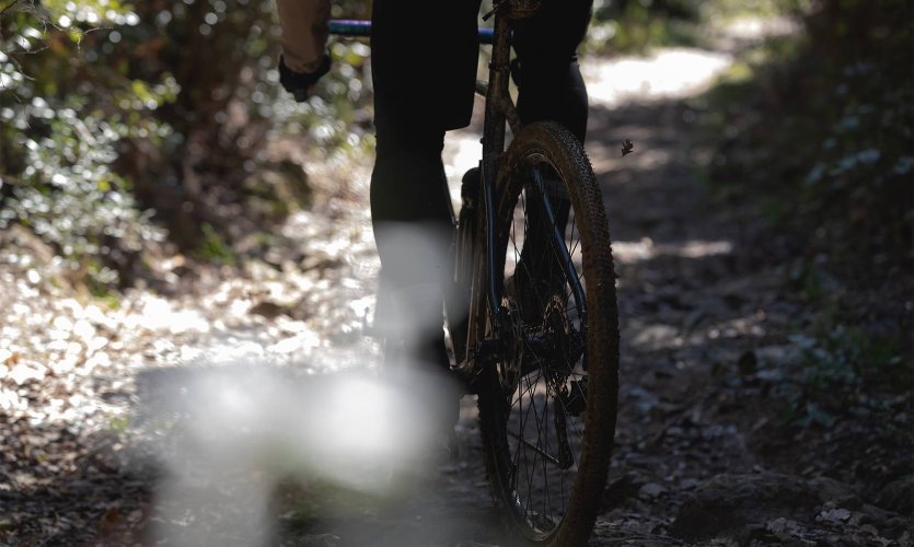 Roue arrière d’un vélo gravel sur un chemin forestier caillouteux légèrement humide, profil du pneu sali par la boue.