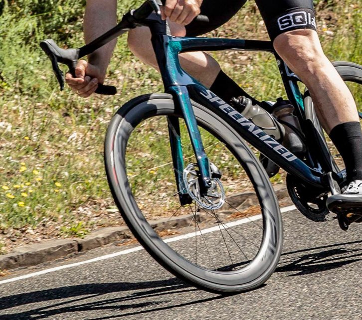 Markus, del servicio de atención al cliente de bc, en una Specialized Tarmac cuesta abajo en una curva. El foco de la imagen se concentra en la rueda delantera de su bicicleta.