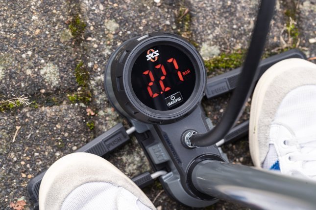 Detailfoto, das digitale Manometer einer SKS Standpumpe. Zwei Füße in weißen Sneakern stehen auf den Fußrasten der Pumpe