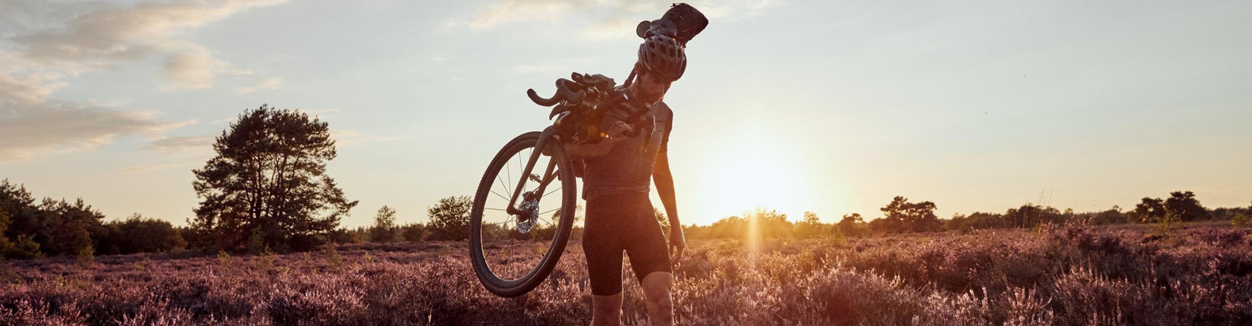Graveler trägt sein Bike im Sonnenuntergang durch die Heide
