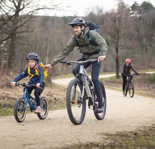 A child is mountain biking with an adult. They are on a gravel path.