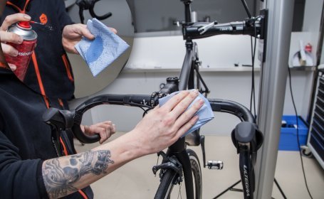 Der Mechaniker sprüht Reiniger auf ein Tuch und wischt den Lenker damit ab. 