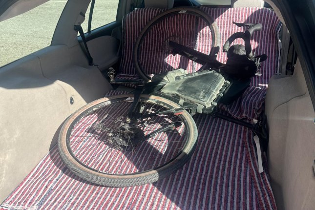 Ein staubiges, graues Gravel-Bike mit Rahmentaschen liegt im Laderaum eines Kombi auf einer rot-weiß-gestreiften Decke