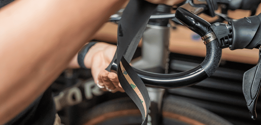 Die Mechanikerin setzt das Lenkerband unterhalb des Lenkers an, die Klebefläche zeigt nach oben zum Lenker. 