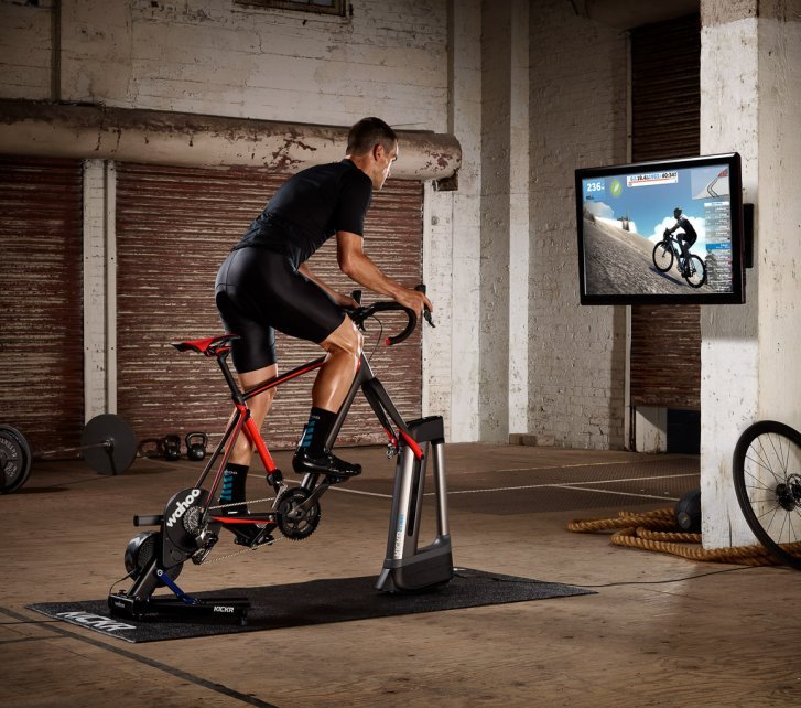 Un hombre entrena en una antigua nave industrial en un smart trainer con un simulador de inclinación.