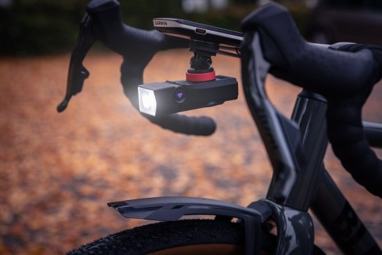 A bicycle front light is mounted hanging below the bike computer on the cockpit of a gravel bike.