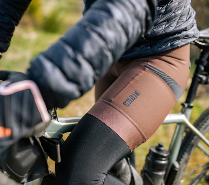 Detailfoto: Wir sehen das linke Bein einer Frau auf einem Gravelbike. Eine braune Bike-Shorts mit Gobik Logo ist im Fokus.
