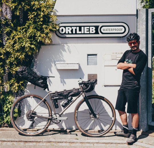 Andi steht samt Gravelbike an der Pforte von ORTLIEB.