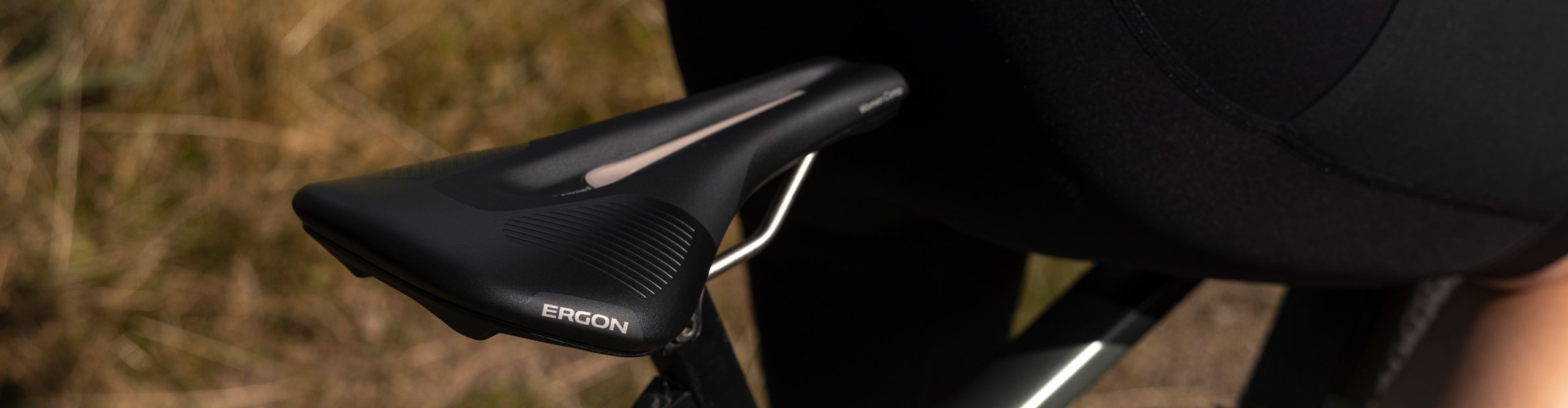 Nahaufnahme eines schwarzen Ergon SR Allroad Woman Fahrradsattels am Rennrad oder Gravelbike, daneben eine Fahrerin in Radhose.