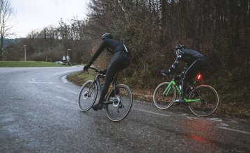 Stephan et Sebastian, du service clientèle de bc, roulent sur une route mouillée par la pluie avec leurs vélos de route. 