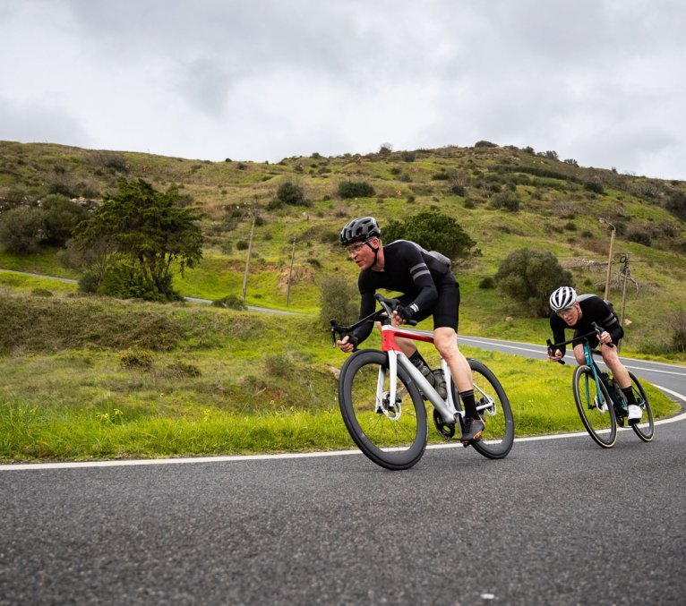 Markus and Sergej from the bc Service department ride downhill through a serpentine pass on Cannondale road bikes.