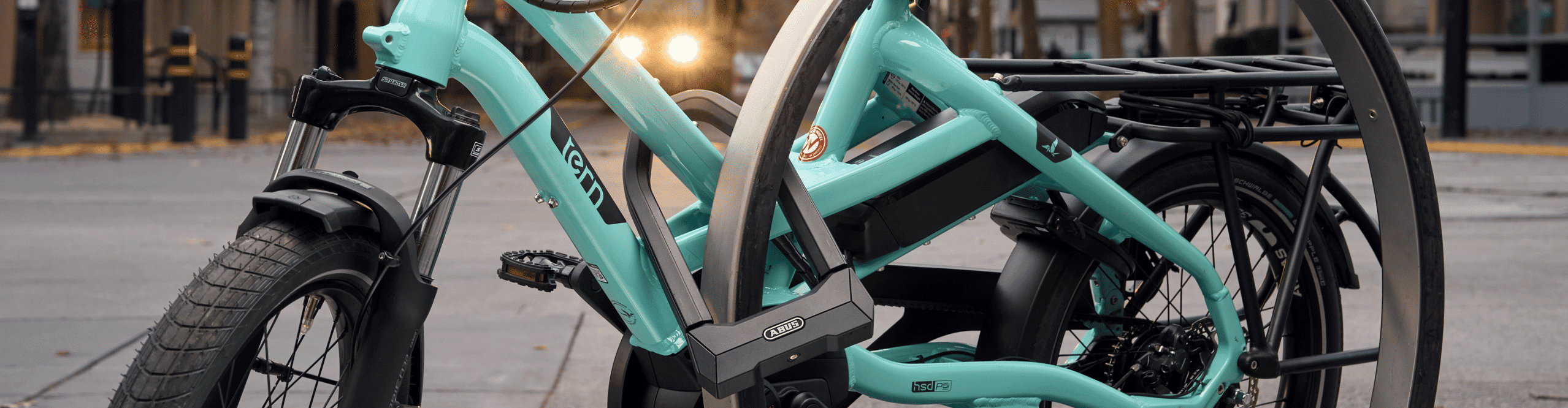 Turquoise Tern electric cargo bike secured to an urban bike rack with an ABUS U-lock.
