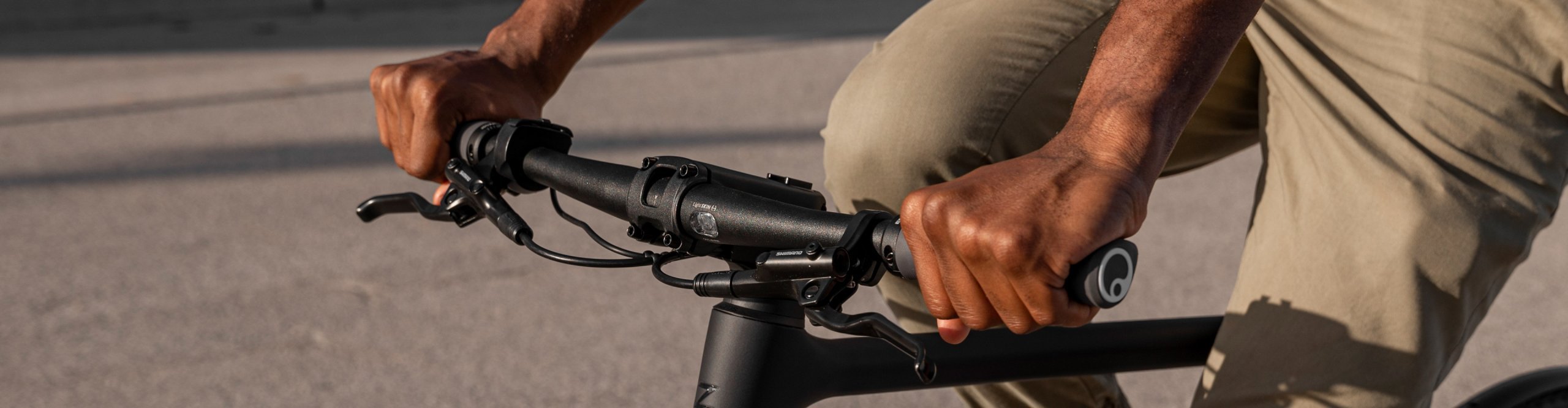Nahaufnahme eines Fahrers mit Ergon Fahrradgriffen am Lenker eines Fitnessbikes auf Asphalt.