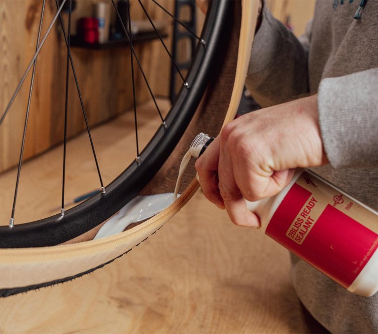 Main versant du liquide préventif tubeless dans un pneu de vélo monté sur une jante, gros plan lors d’une conversion en tubeless.
