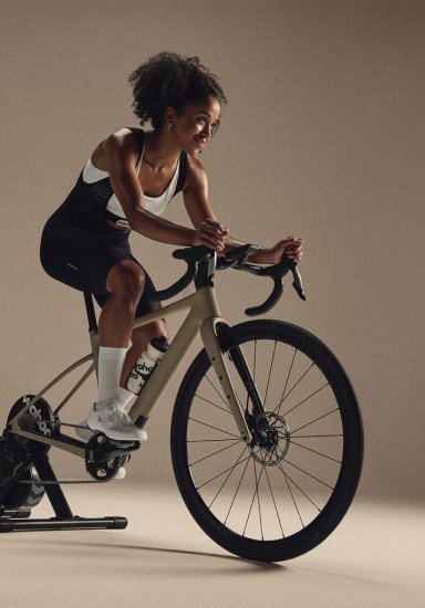 Sportliche Frau trainiert auf einem Rennrad, das auf dem Wahoo KICKR Core V2 Rollentrainer montiert ist, in einem minimalistischen Indoor-Setup.