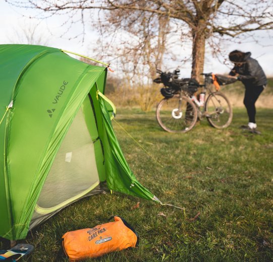 Christian, du service clientèle de bc, prépare sa sacoche de selle. Au premier plan se trouve sa tente, à côté de laquelle se trouve un sac Ortlieb.