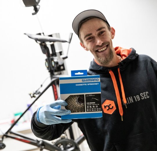 Thomas, mécanicien chez bc, tient une nouvelle cassette Shimano à 11 vitesses devant l’appareil photo. 