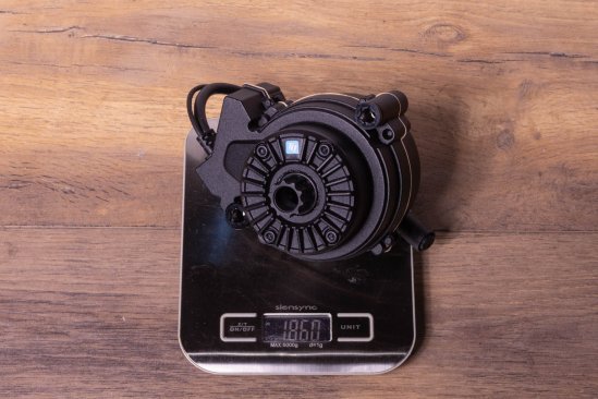 A TQ HPR50 e-bike drive on a kitchen scale on a dark wooden floor. Display shows 1,860 grams