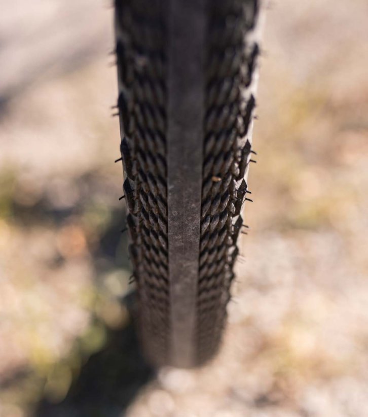 Vue frontale d’un pneu gravel semi-slick avec bande centrale lisse et crampons latéraux pour plus d’adhérence.