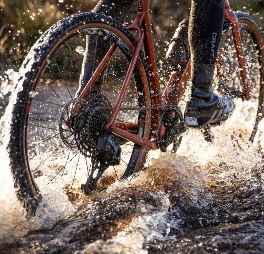 A biker rides through a large puddle.