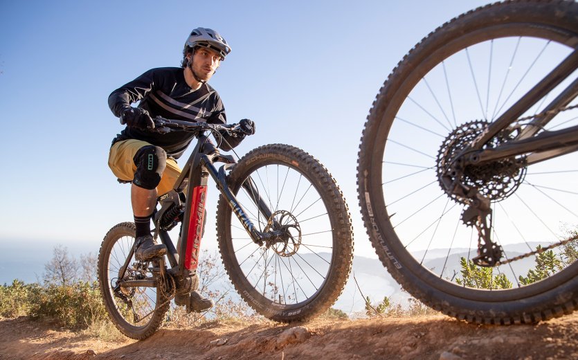 Zwei Mountainbiker, einer davon auf einem Liteville 301 E-Bike, fahren bei sonnigem Wetter in der Nähe der Küste über einen Trail.