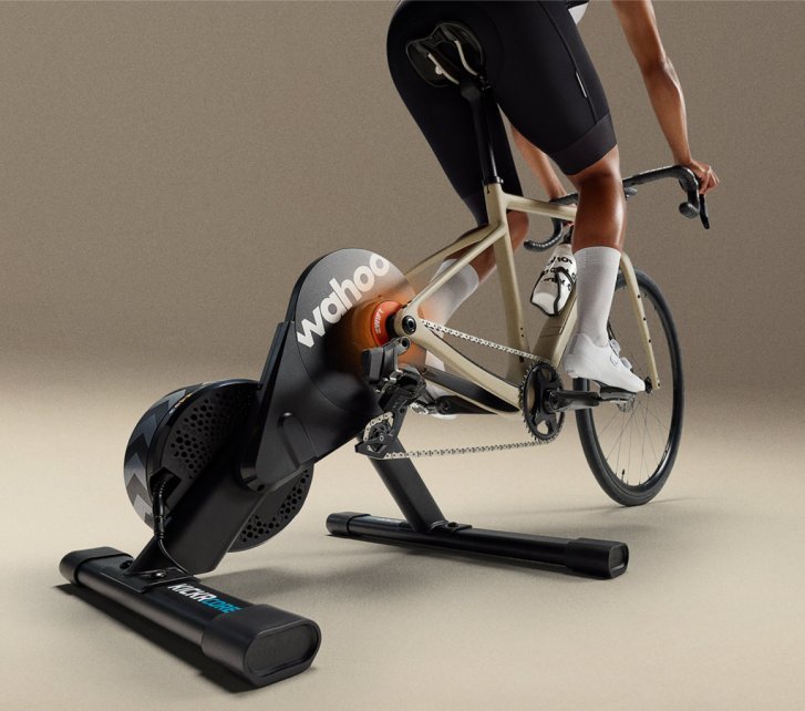 Un vélo de course est monté sur le home trainer Wahoo KICKR Core avec Zwift Click & Cog, tandis qu'une personne s'entraîne en salle dans un environnement de studio.