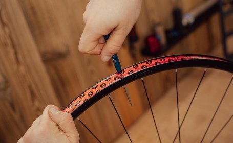 Hand durchsticht das Felgenband über dem Ventilloch mit einer spitzen Werkzeugspitze.