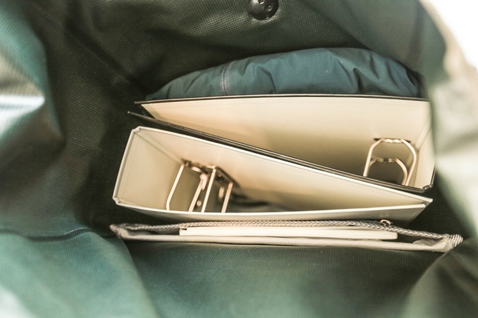 Innenansicht der Ortlieb Back Roller Urban Fahrradtasche, die einen weißen Organizer mit mehreren Fächern und Metallringen zeigt, gefüllt mit einer grünen Hülle und einer grauen Netztasche.